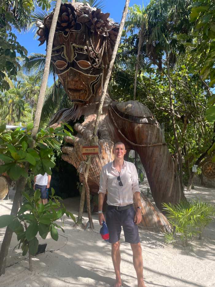 Ladislas Maurice standing in front of wooden statue in Tulum